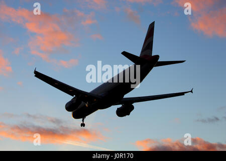 Large airliner landing at London Heathrow airport silhouetted against a sunset sky Stock Photo