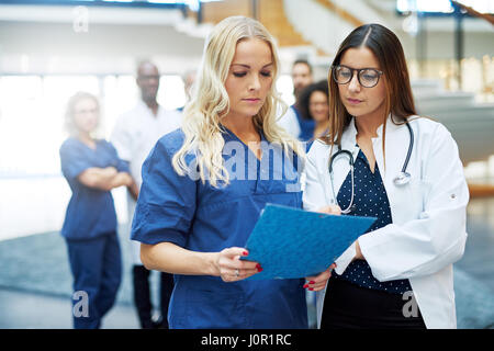 Two young female medics standing in the clinic and looking through the documents. Stock Photo