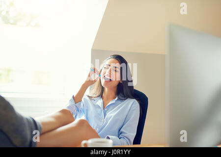 Single female workaholic with funny expression brushing teeth at desk with feet up on top Stock Photo