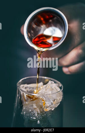 Bartender is pouring alcohol from a measuring glass into a glass over ice Stock Photo