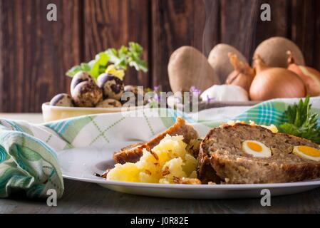 Horizontal photo with two slices of homemade Easter meatloaf which is filled by quail eggs and is served with meshed onion potatoes on white plate. In Stock Photo