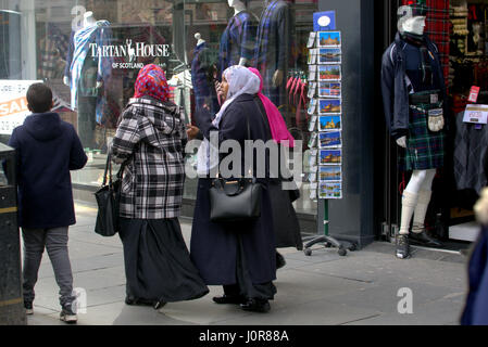 Asian African refugee dressed Hijab scarf on street in the UK everyday scene family walking in crowd with Scottish tartan memorabilia atound Stock Photo