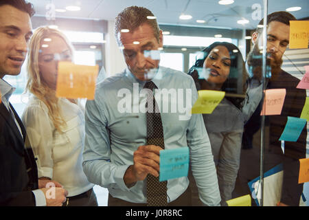 Multiethnic businessteam in office working on a strategy for the startup. Standing meeting brainstorming using sticker posters on wall Stock Photo