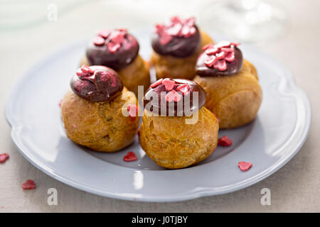 Choux pastry profiteroles with mousse topped with chocolate decorated with heart shaped candies Stock Photo