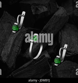 Ring and earrings with emeralds on the background of coal Stock Photo