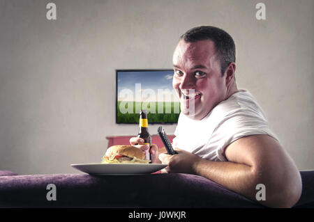 Fat man with beer and hamburger in front of TV Stock Photo