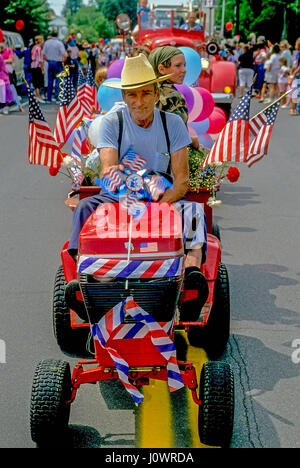 Man in a straw hat drives a mini tractor decorated with American flags in a 4th of July parade in Plainfield, New Hampshire, United States. Stock Photo