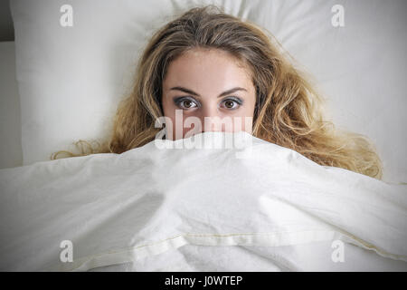 Young blond woman hiding under the sheets Stock Photo