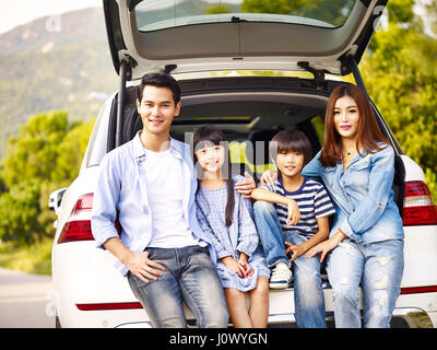 happy asian family with two children posing with the car in which they are traveling. Stock Photo