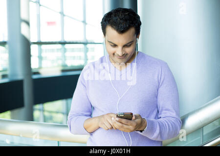 Closeup portrait, young happy man in purple sweater standing, checking his cellphone, listening to music, watching movie, isolated on interior office  Stock Photo