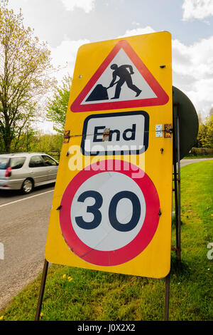 Temporary speed restriction end of road works sign showing 30 miles per hour limit used in the United Kingdom with defocussed traffic Stock Photo