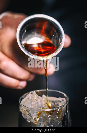 Barman is pouring alcohol from a jigger into a glass over ice; preparing an alcoholic cocktails Stock Photo