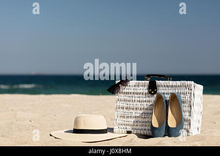 Summer vacation at sea. White wicker suitcase and women's accessories and shoes on the beach. Selective focus. Stock Photo