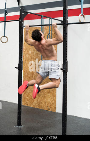 Rear angled young of athletic young man doing pull ups in gym, toned physique Stock Photo