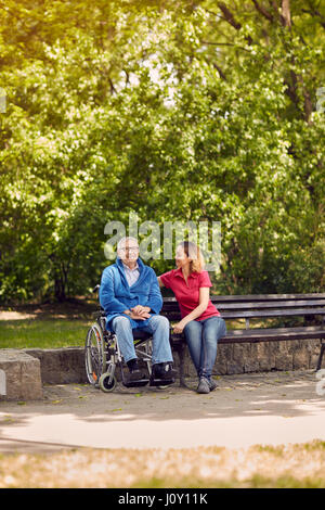 Spending time together cheerful daughter with her disabled father in wheelchair in the park Stock Photo