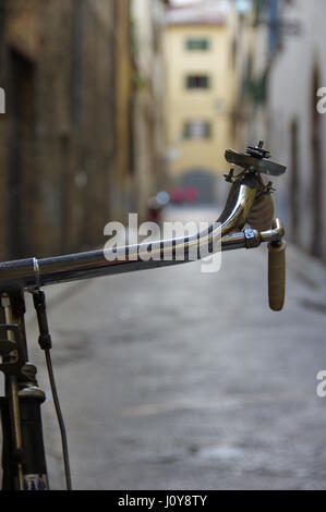 Bicycle handlebar detail against a bokeh alley in central Florence (Firenze), Tuscany, Italy, Europe - Selective focus on handlebars Stock Photo