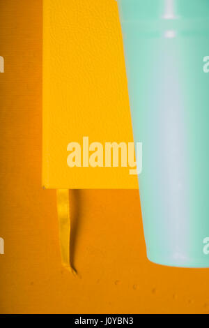 Yellow notepad and plastic turquoise glass on a yellow background Stock Photo