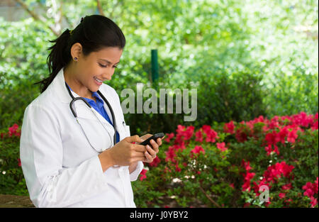 Closeup portrait, friendly, young smiling confident female doctor with stethoscope, healthcare professional texting on phone, isolated outside green t Stock Photo