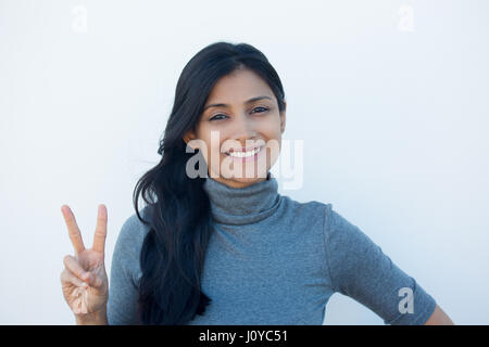 Closeup portrait, young, happy, smiling, confident, excited woman giving peace victory, two sign gesture, isolated white wall background. Positive emo Stock Photo