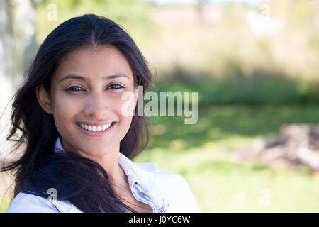 Closeup portrait of confident smiling happy pretty young woman in gray suit, isolated background of blurred trees. Positive human emotion facial expre Stock Photo