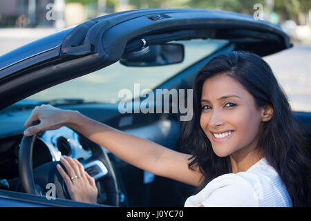 Closeup portrait young smiling, happy, attractive woman smiling from behind in her brand new sports car drop top, hand on steering wheel, isolated out Stock Photo