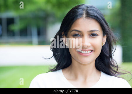 Closeup portrait of confident smiling happy pretty young woman in white shirt, isolated background of blurred trees. Positive human emotion facial exp Stock Photo