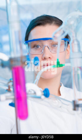 Attractive young female scientist working in laboratory.  Woman scientist looking at a red test tube in a lab. Young woman in chemical lab Stock Photo