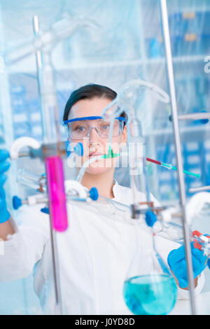 Attractive young female scientist working in laboratory.  Woman scientist looking at a red test tube in a lab. Young woman in chemical lab Stock Photo
