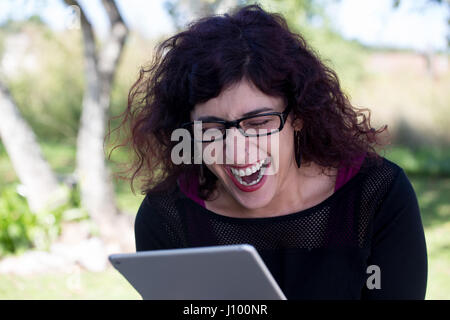 Closeup portrait, happy woman in black shirt and glasses using silver pc, isolated outdoors background. Positive human emotion facial expressions feel Stock Photo