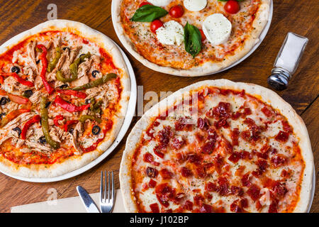 Several different pizzas on a wooden restaurant table. Stock Photo