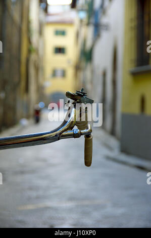 Bicycle handlebar detail against a bokeh alley in central Florence (Firenze), Tuscany, Italy, Europe - Selective focus on handlebars Stock Photo