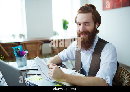 Happy designer with earphones reading papers in design studio Stock Photo