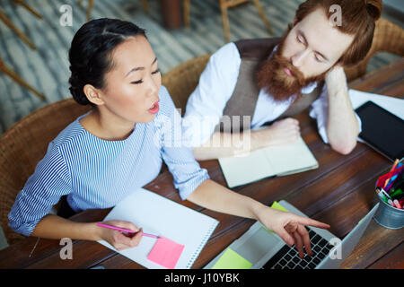 Young woman pointing at laptop display and explaining her choice of data for new creative project Stock Photo