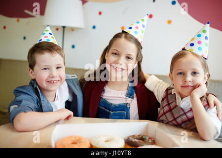 Happy kids in birthday-caps relaxing in cafe Stock Photo