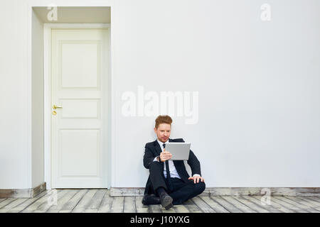 Portrait of handsome young businessman using tablet computer sitting on floor of empty office room Stock Photo
