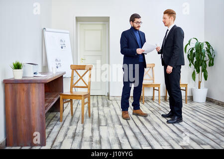 Portrait of two colleagues standing in office and talking, discussing documents and work issues Stock Photo