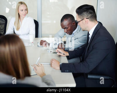 Multi-ethnic group of business people meeting in conference room: discussing corporate issues and using smartphone at table Stock Photo