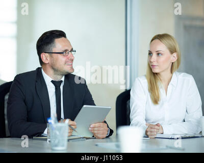 Portrait of middle-aged businessman presenting ideas in meeting, holding digital tablet and talking to his colleagues Stock Photo