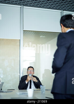 Portrait of middle-aged businessman using smartphone while listening to employee across the meeting table Stock Photo