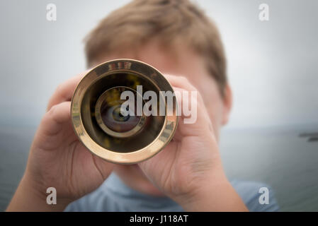 Boy standing by ocean looking through a telescope Stock Photo
