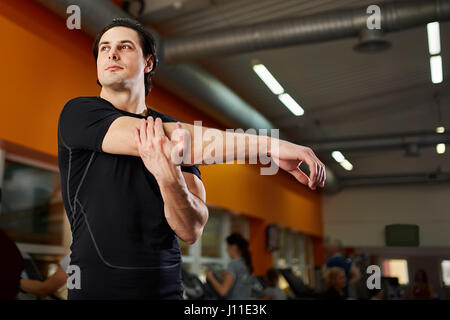 Young athlete healthy man in the black sportwear stretching shoulder before gym workout. Portrait of attractive sportsman. Horizontal cpose-up photo.  Stock Photo