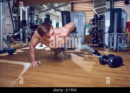 Sports guy does push-ups from the floor on one hand in  gym Stock Photo