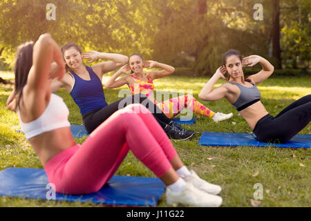 Beautiful girlfriends doing sit-up in the park with female fitness trainer. Selective focus. Stock Photo