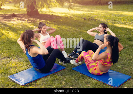 Four beautiful female friends doing doing sit-up in the park. Stock Photo