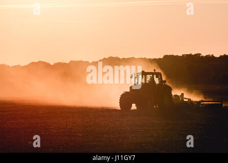 Silhouette of tractor working on a farm at twilight Stock Photo