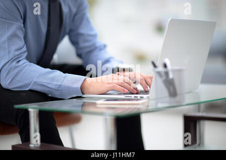 Young business man working on a laptop at his desk in the office, in view of the profile against the window Stock Photo