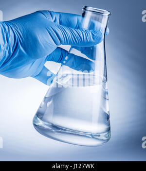 Laboratory beaker in analyst's hand in plastic glove. Stock Photo