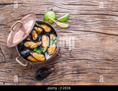 Boiled mussels in copper pan on the wooden table.