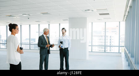 Business people standing at empty space discussing the interior of office with architect. Real estate agent talking with potential clients inside an e Stock Photo