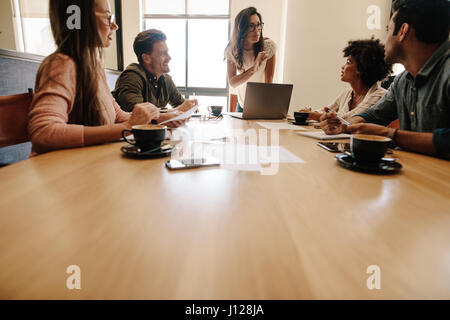Young woman discussing with group of executives sitting around a table. Multi ethnic business team meeting in conference room. Stock Photo